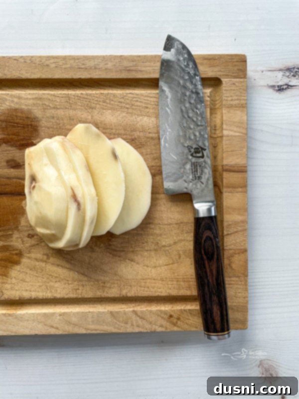 Top view of peeled, sliced potato on wooden cutting board with knife, emphasizing the consistent fry shape.