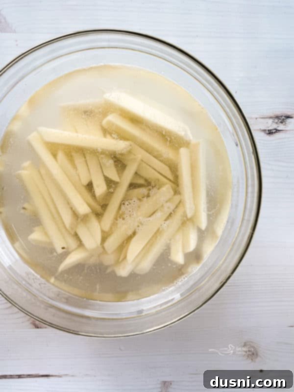 Seriously Crispy Homemade Double-Fried Fries 10 Bowl of peeled and cut fries in bowl of cold water, showing the soaking process.
