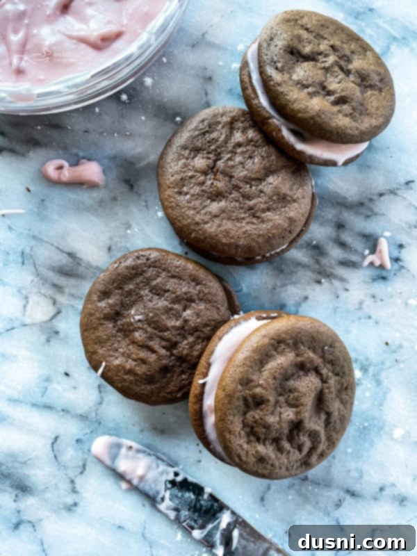 Several assembled chocolate strawberry whoopie pies with pink filling on a baking sheet