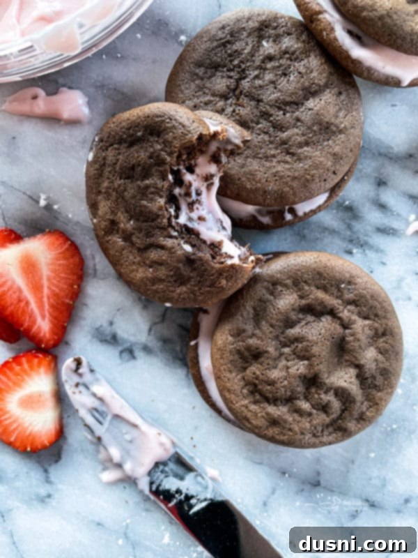 Close-up of a chocolate strawberry whoopie pie with a bite taken out, revealing the pink strawberry cream filling
