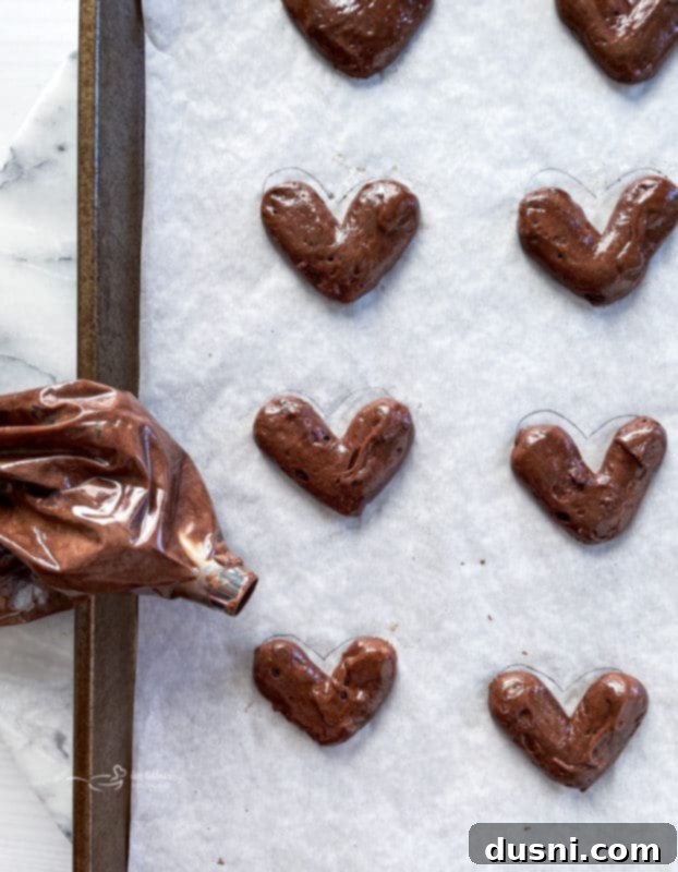 Piping heart-shaped chocolate whoopie pie batter onto parchment paper, showing spacing