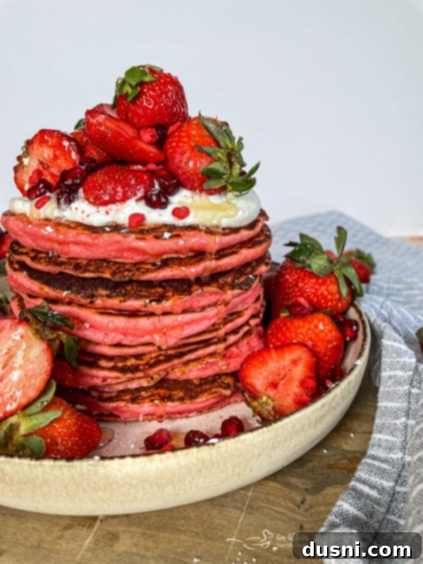 A stack of golden brown pancakes with fresh strawberries and whipped cream on top, on a white plate.