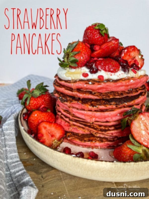 A stack of strawberry pancakes with fresh strawberries on top.