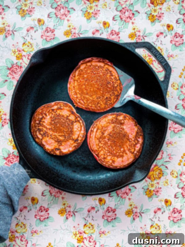 Pancake batter being poured onto a hot griddle to form pancakes.