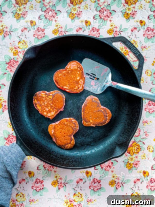 Heart-shaped pancakes cooking on a griddle, bubbles forming.