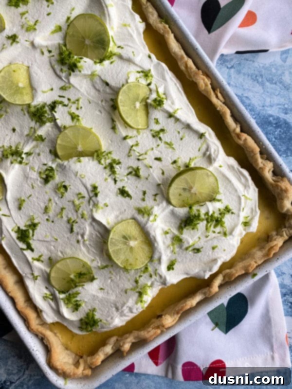 Zesty Key Lime Sheet Pie 13 Key Lime Slab Pie with whipped cream, garnished with fresh lime slices and zest.