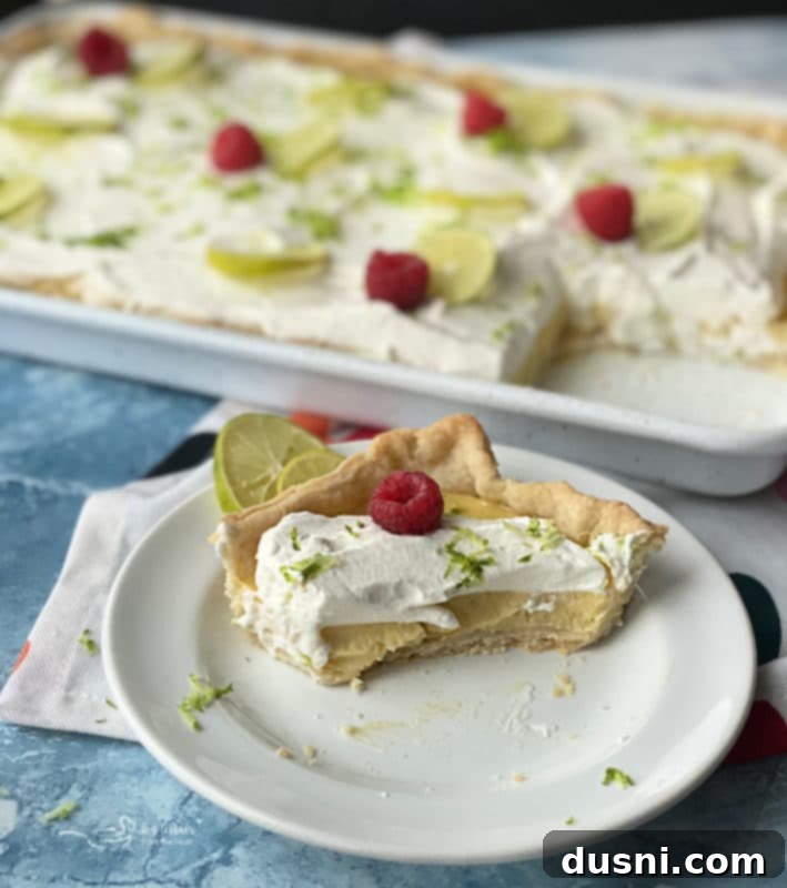 Zesty Key Lime Sheet Pie 3 Close-up of Key Lime Slab Pie slice showing the golden crust, yellow custard, and white whipped cream with raspberries.