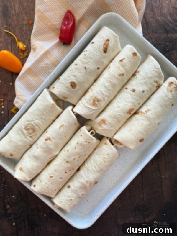 Rolled breakfast burritos on a baking sheet