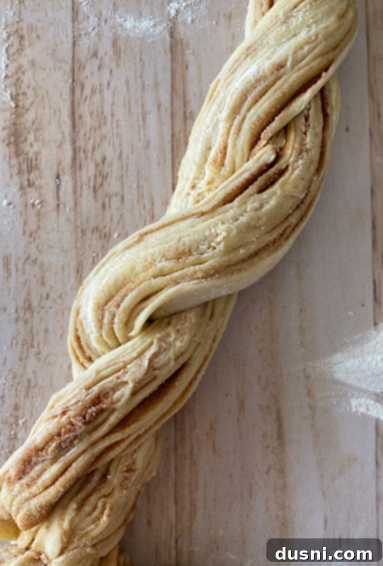 Step-by-step instruction showing the rolled dough log sliced lengthwise, exposing cinnamon layers