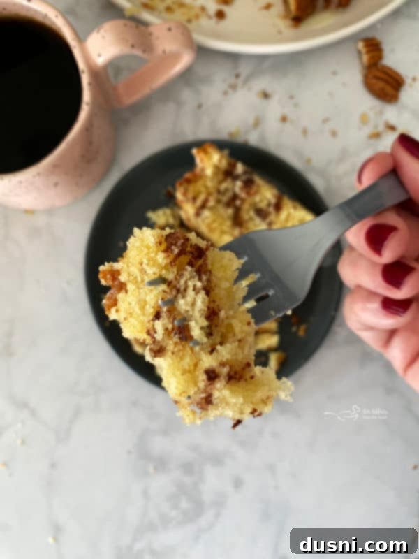 A slice of sour cream coffee cake on a plate with a cup of coffee