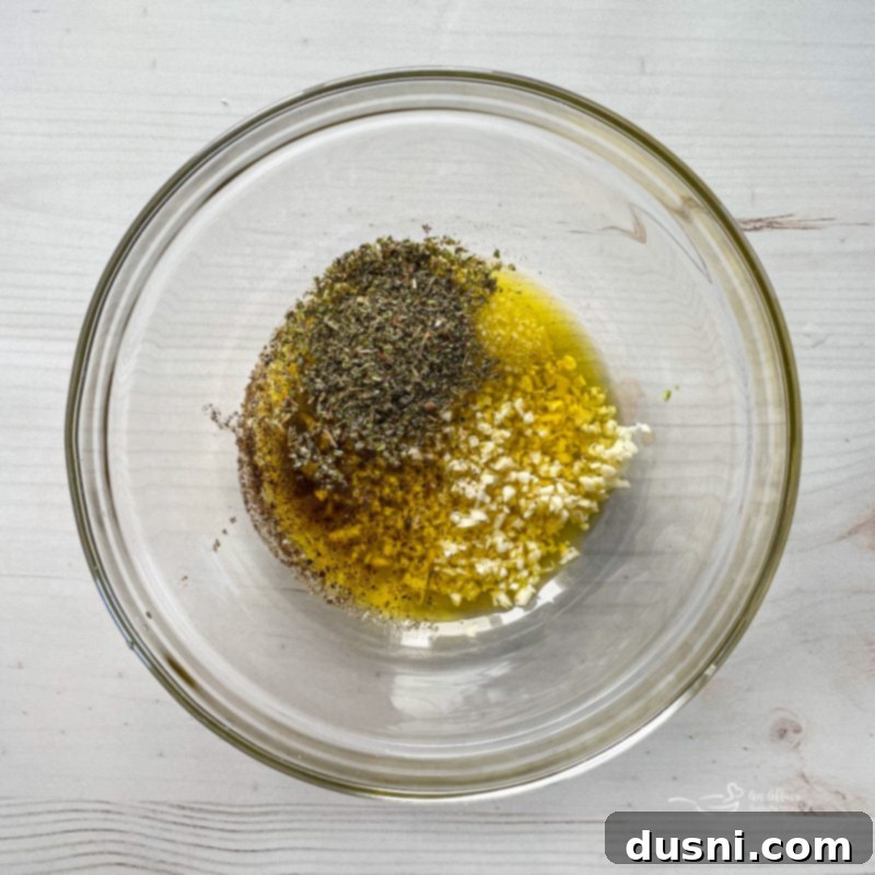 Top view of garlic, olive oil, and seasoning in clear bowl