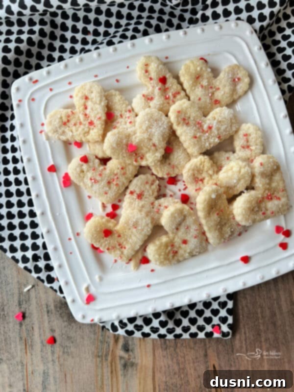 Culinary Anthem Remix 3 Close up of Heart shaped pie crust cookies with red sprinkles on a white, square dish.