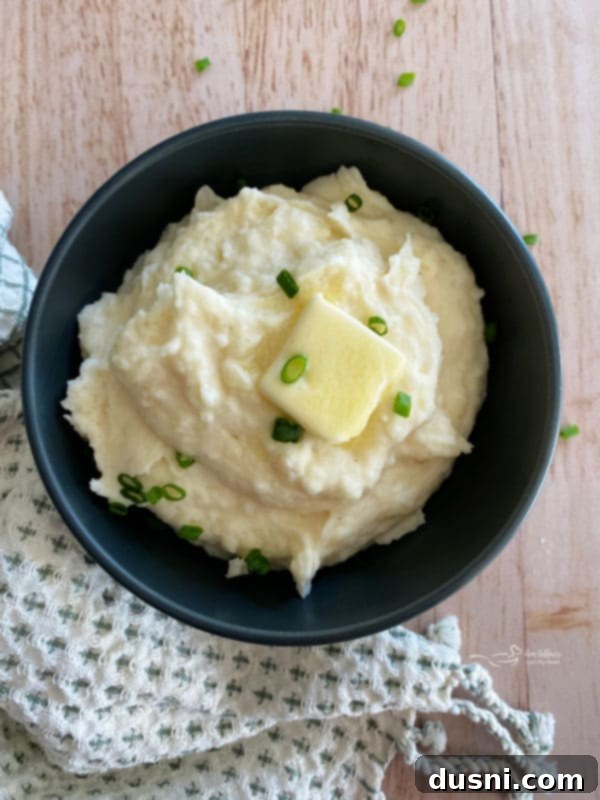 Ultimate Creamy Slow Cooker Mashed Potatoes 2 Top view of mashed potatoes in black bowl with chives and butter, garnished beautifully
