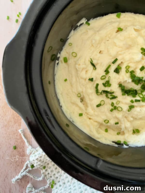Ultimate Creamy Slow Cooker Mashed Potatoes 3 Top view of mashed potatoes in the Crockpot with chives and a spoonful of melted butter