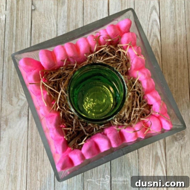 A closer look at a partially assembled Peep Centerpiece, showing how marshmallow Peep bunnies are arranged around a central mason jar on top of jelly beans.