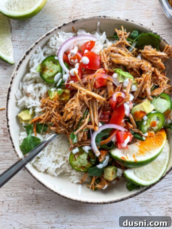 A vibrant bowl of Slow Cooker Cilantro Lime Pork, garnished with fresh limes, tomatoes, red onions, rice, and jalapeños, ready to be enjoyed as a hearty meal.