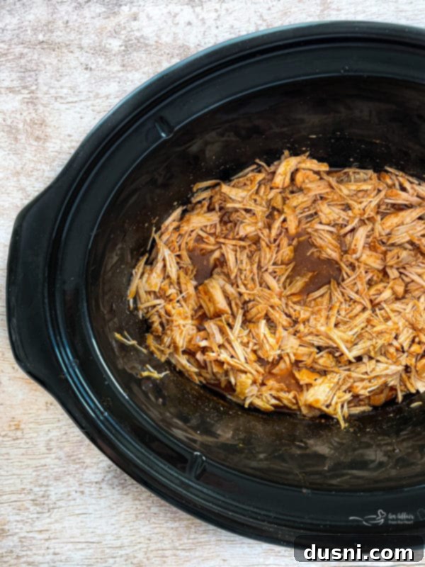 Top-down view of the slow cooker cilantro lime pork simmering in the Crockpot, showcasing the tender meat in its rich cooking liquid.