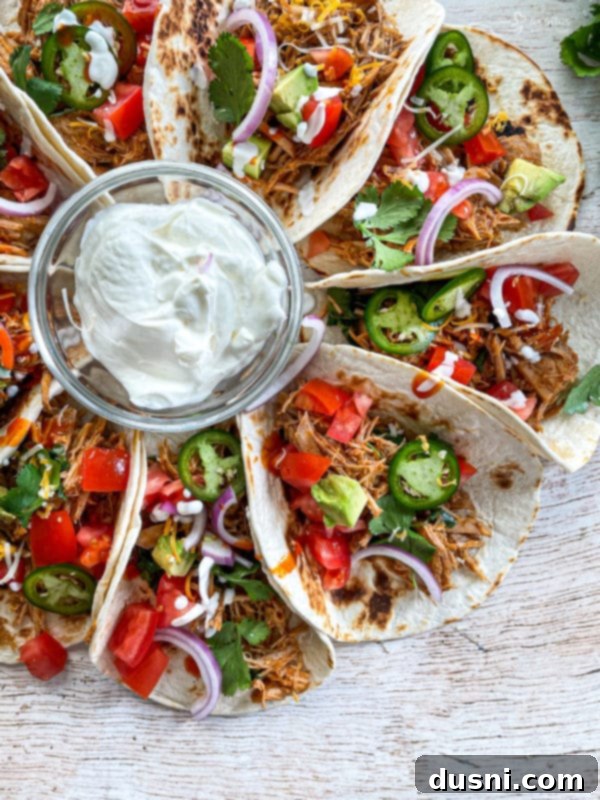 A close-up top view of two tacos generously filled with slow cooker cilantro lime pork, garnished with fresh cilantro and a squeeze of lime.