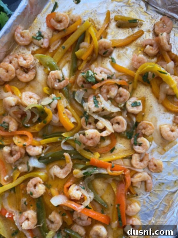 Cooked sheet pan shrimp fajitas mixed with vegetables, glistening with cilantro lime butter.