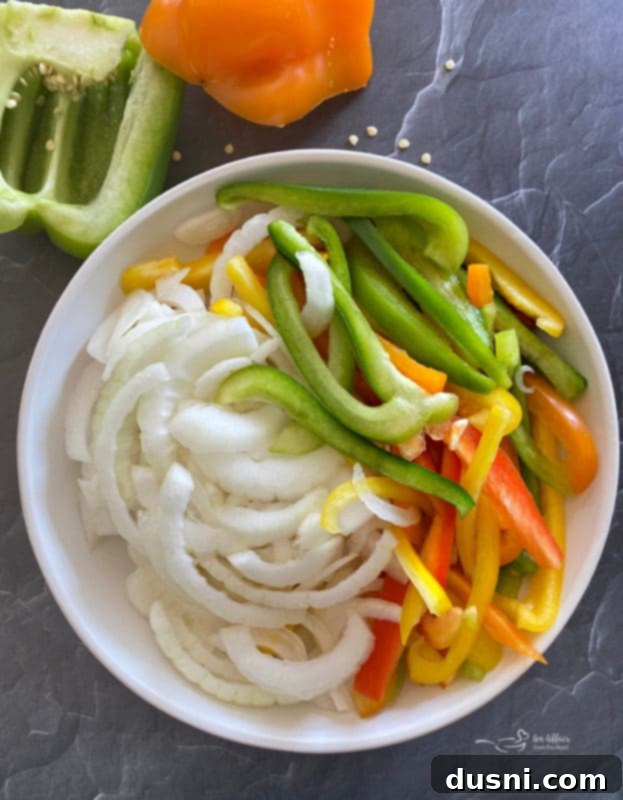 Sliced colorful bell peppers (red, yellow, green) and onions on a cutting board.