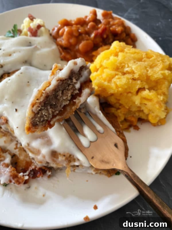 A fork piercing a piece of country fried steak, showcasing its crispy texture, with savory gravy drizzled over it