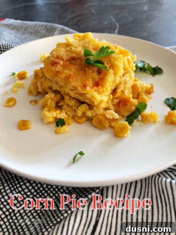 A comforting individual serving of golden brown corn pie casserole on a white plate, garnished with fresh parsley