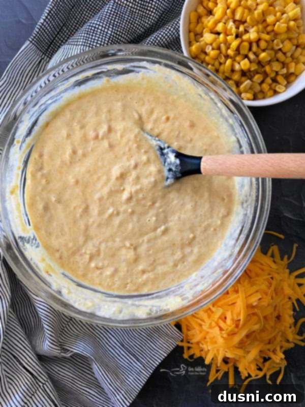 A bowl of creamy corn pie mixture, ready for cheese and corn additions, stirred with a spoon