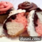 Classic Neapolitan Swirl Cupcakes 2 Neapolitan Cupcakes and one cut in half on a white surface, showcasing the three distinct layers and frosting.