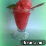 Refreshing Watermelon Bliss 2 Vibrant watermelon sorbet in a sundae glass, with a spoon resting in it, ready to be enjoyed. The texture appears smooth and inviting.