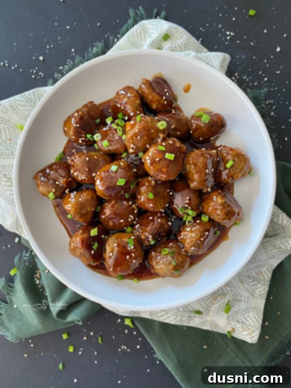 Close-up of Sticky Asian Meatballs garnished with green onions and sesame seeds