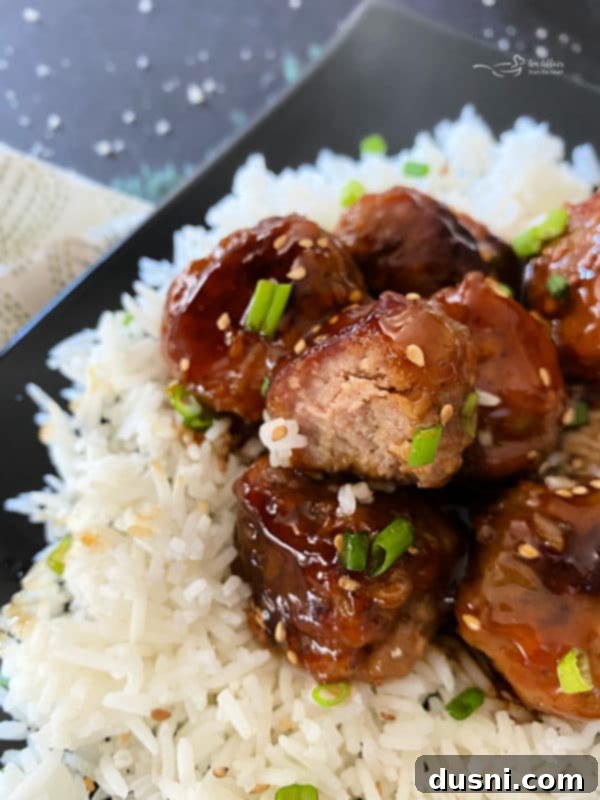 Sticky Asian Meatballs served over white rice on a black plate