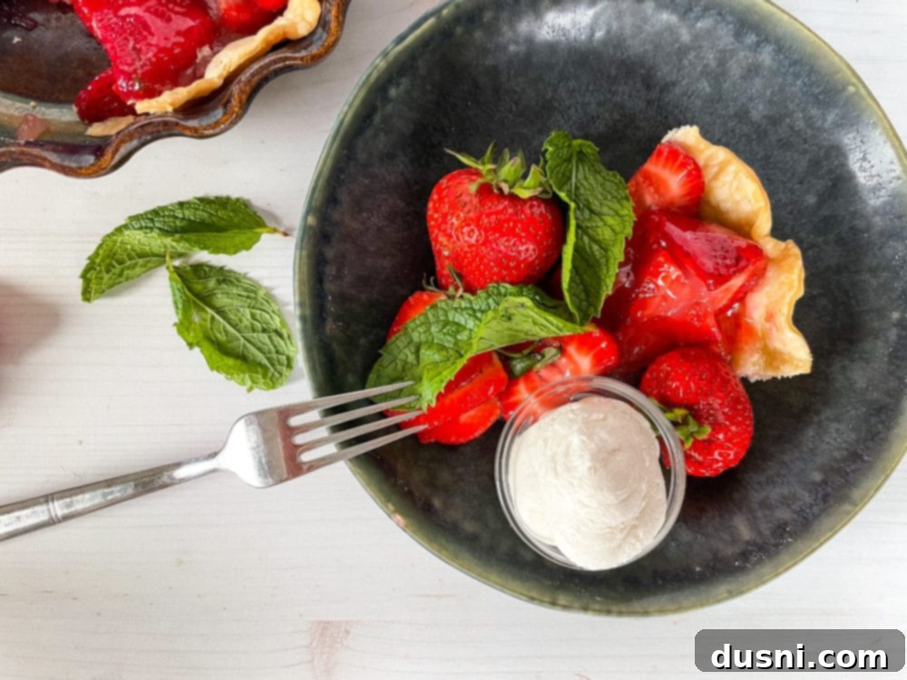 Top view of a perfect slice of strawberry pie on a plate, topped with a swirl of fresh whipped cream