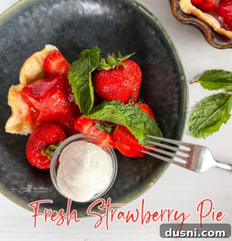 Top view of a generous slice of fresh strawberry pie in a grey bowl, adorned with whipped cream