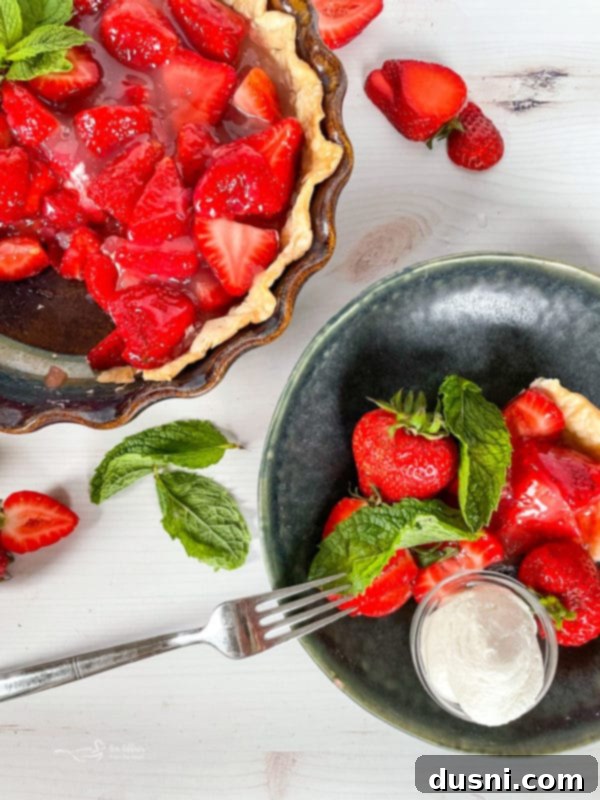 Top view of a freshly baked strawberry pie, with a single slice on a plate adorned with whipped cream and a fork