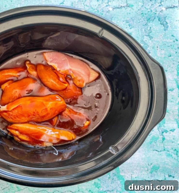 Crockpot Luau Chicken Sandwiches 9 Sauce being poured over chicken breasts in a slow cooker