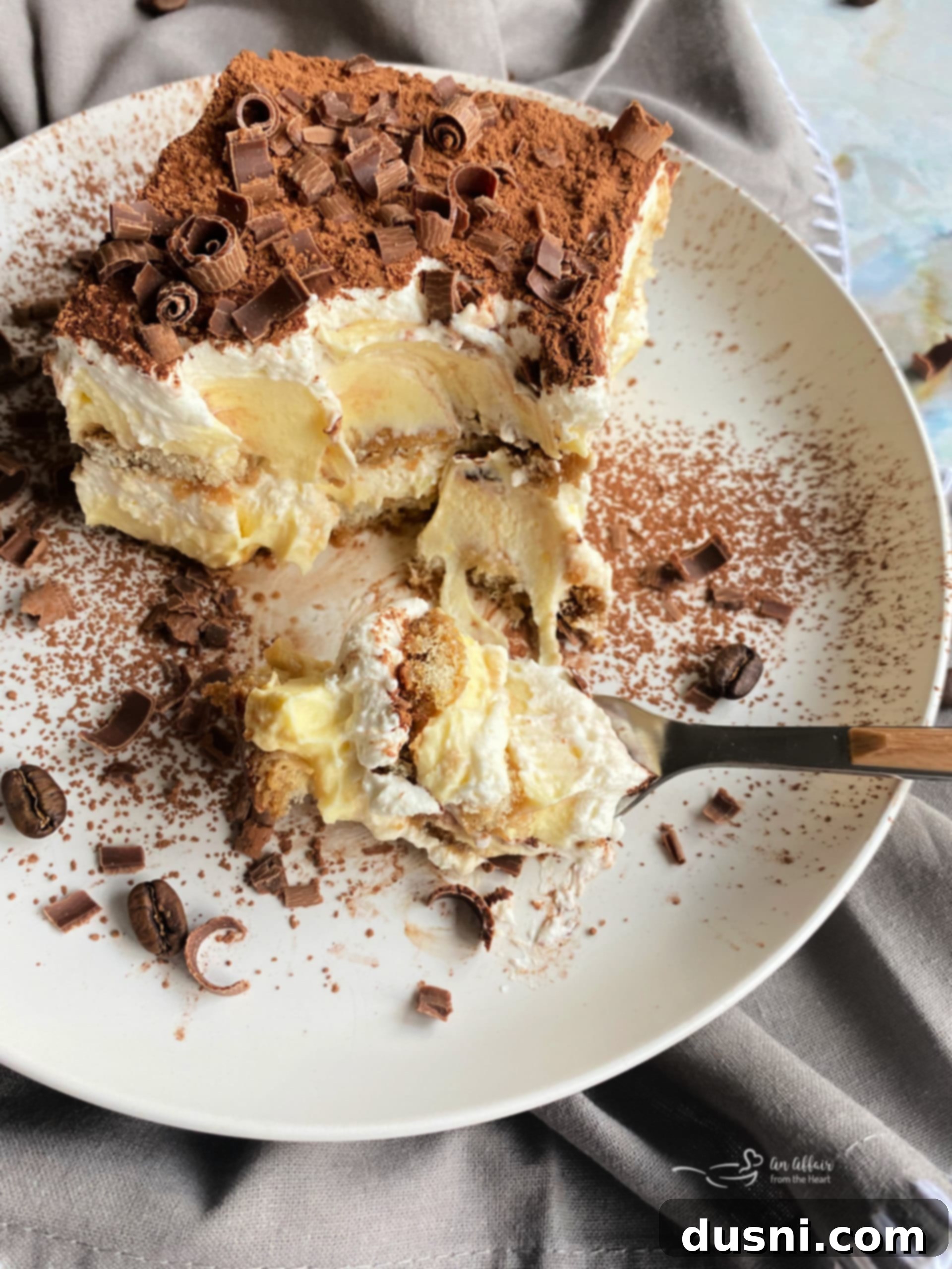 A slice of tiramisu on a plate, topped with cocoa powder and chocolate curls.