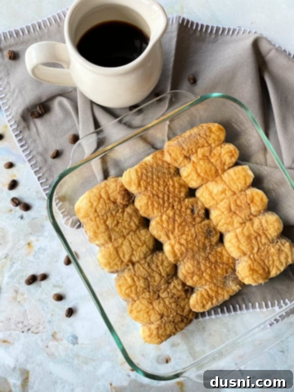 Ladyfingers being drizzled with coffee and rum mixture.