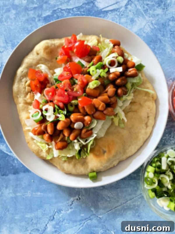 Native Fry Bread Tacos 2 A plate of Indian Tacos with Indian Fry Bread, topped with lettuce, tomatoes, and beans.