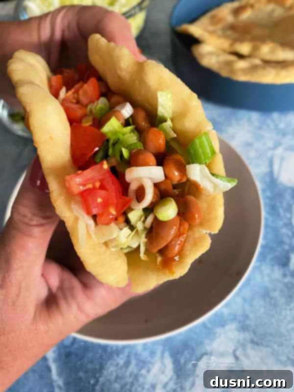 Native Fry Bread Tacos 13 Indian Tacos in fry bread, held in hand, blue background