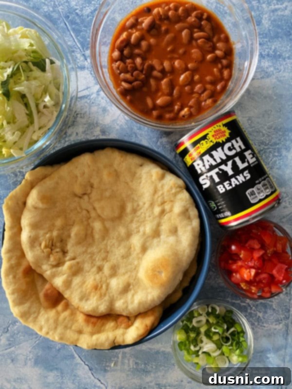 Native Fry Bread Tacos 9 Ingredients for Indian Tacos laid out: fry bread, ranch style beans, lettuce, tomatoes, and green onions.