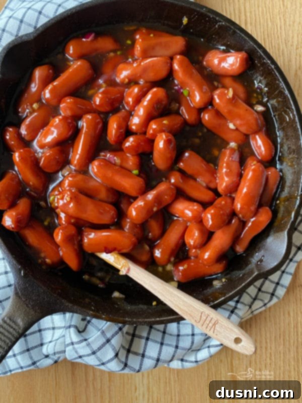 Dorothy's BBQ Little Smokies stirring in a cast iron skillet on a stovetop.