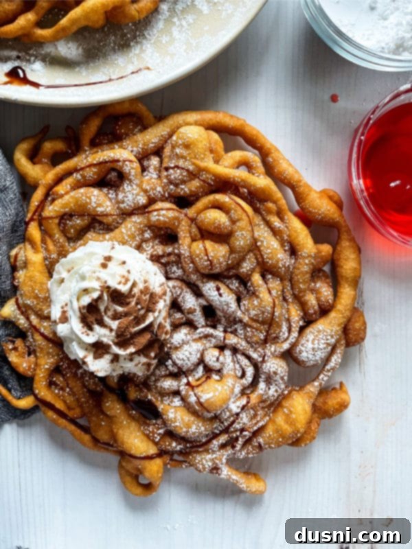 Delicious Funnel Cakes 2 top view of funnel cake on white surface with whipped cream and drizzled chocolate