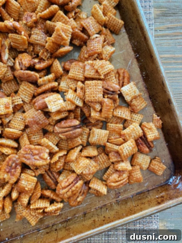 Overhead view of a baking sheet filled with golden-brown praline Chex Mix, freshly baked.