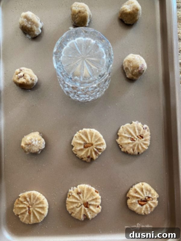 pecan butter cookie dough on baking sheet with designs, glass, and pecans