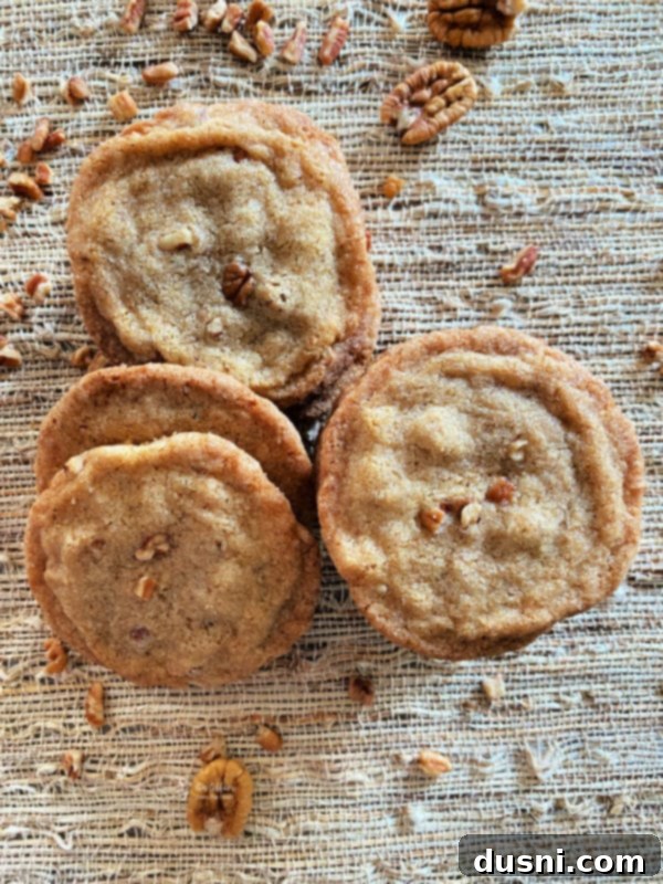 top view of pecan butter cookies on tan surface with pecans