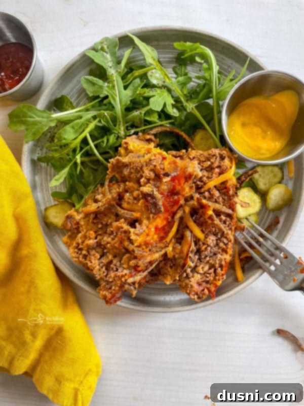 bacon cheeseburger meatloaf on plate with salad and mustard, garnished with pickles and crispy onions