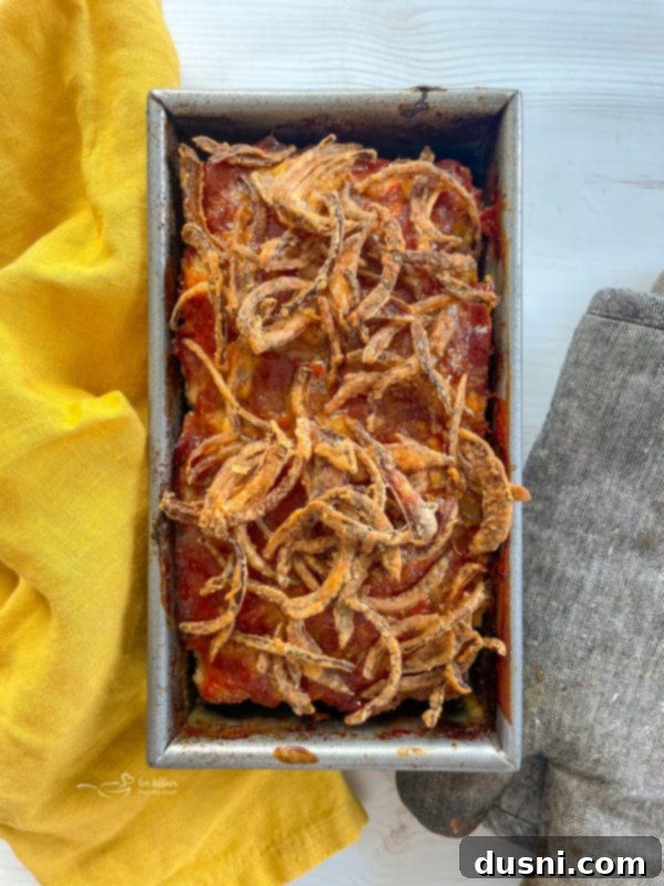 top view of a golden brown meatloaf in a loaf pan, topped with crispy fried onions