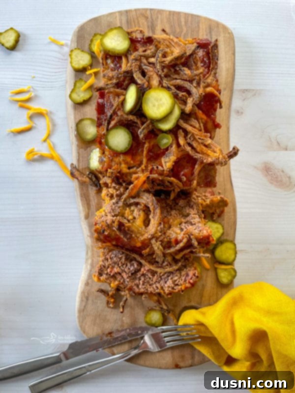 bacon cheeseburger meatloaf topped with fried onions and pickles on a serving platter, ready to be sliced