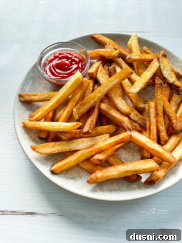 Front view of golden crispy French fries on a plate with a dollop of ketchup
