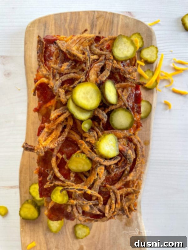 bacon cheeseburger meatloaf topped with fresh pickles and fried onions, ready to serve on a cutting board